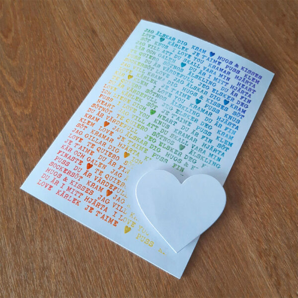 Vit kortbas med kärleksfulla ord stämplade i regnbågens färger, vitt hjärta nere till höger.