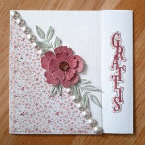 Kvadratiskt grattiskort med blommigt mönstrat papper i en triangel, ljusa pärlor och en stor rosa blomma.